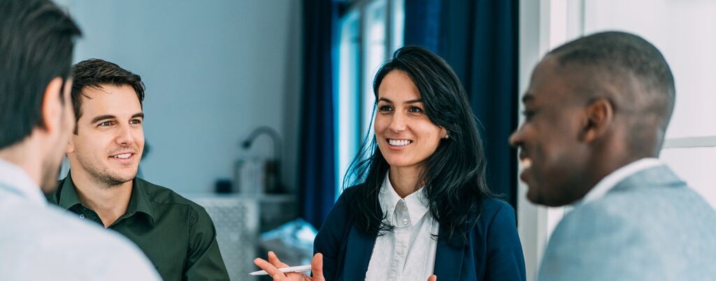 Diverse group of business professionals smiling and discussing ideas around a conference table during a team meeting in a modern office.
